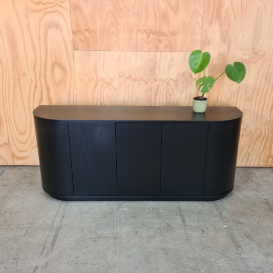 Black rectangular object on a wooden surface with a plant