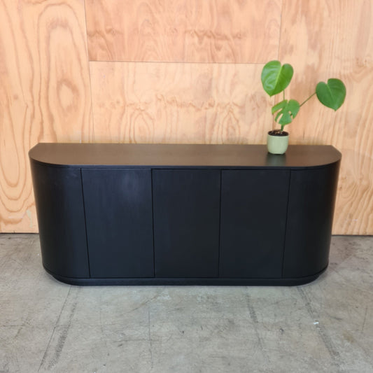 Black rectangular object on a wooden surface with a plant