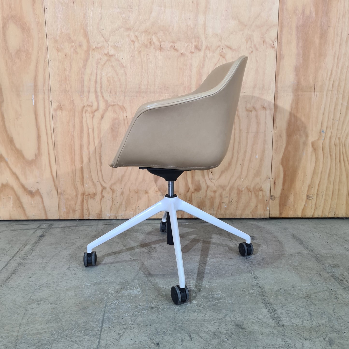 Beige office chair with white frame on a wooden floor and concrete wall.