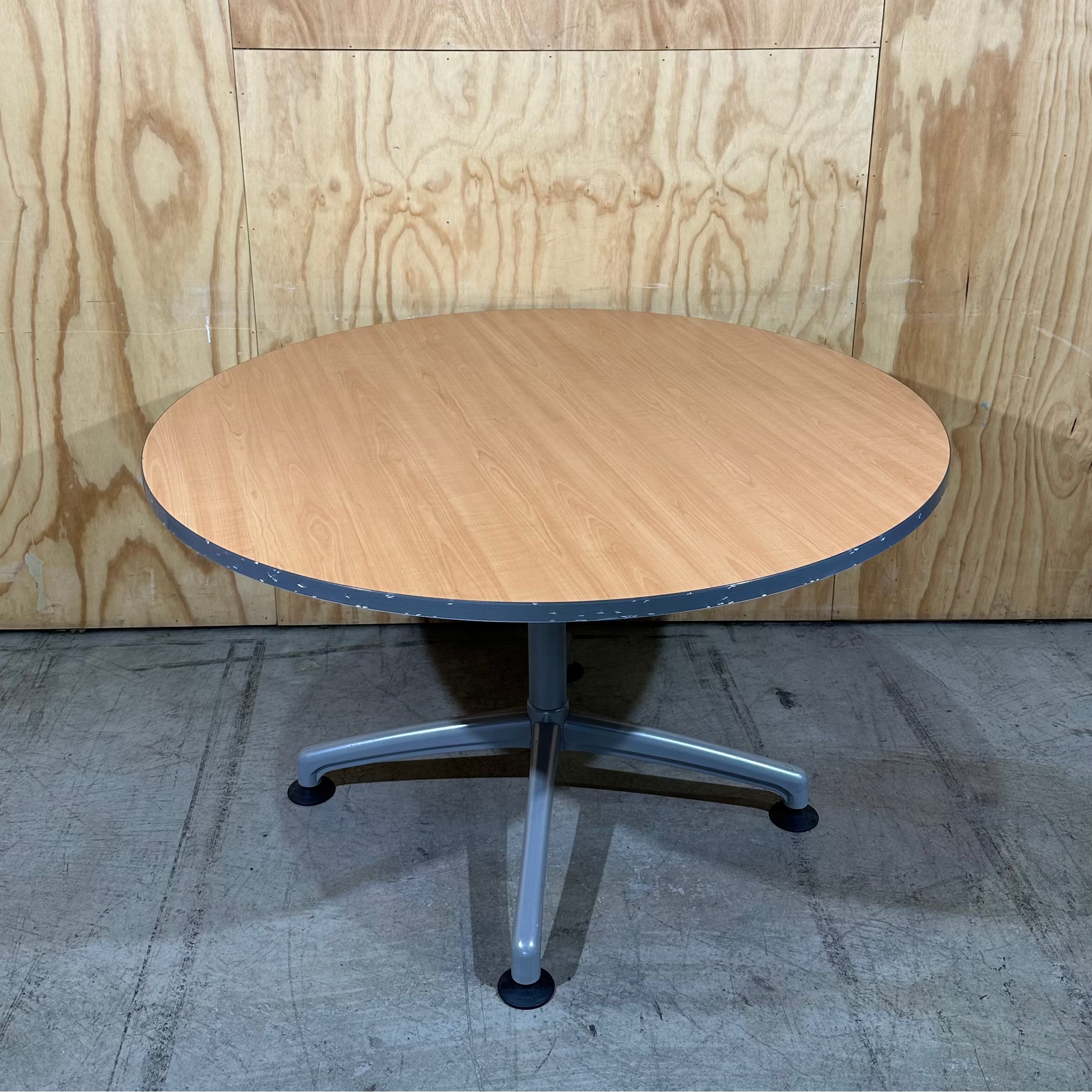 Round wooden table with metal base against a wooden panel background