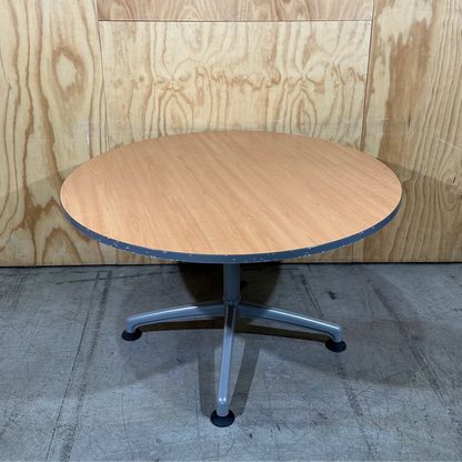 Round wooden table with metal base against a wooden panel background