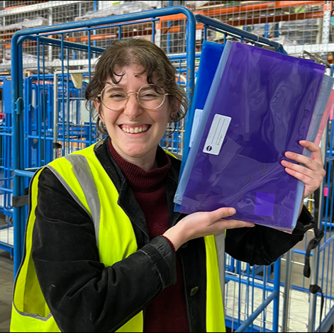 Maddison holding folders in high vis in braybrook green collect warehouse with trolley cage collection service in background
